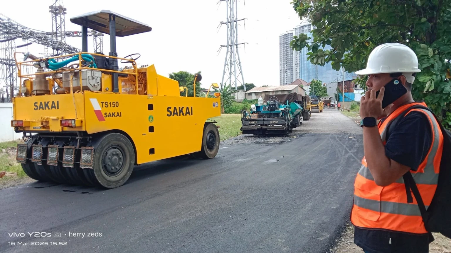Pekerjaan pengaspalan jalan dengan alat berat dan petugas lapangan